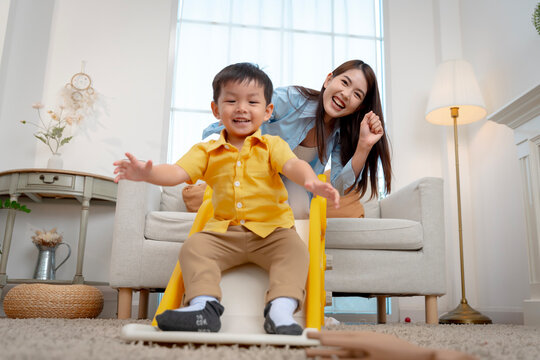 oyful little boy sliding down indoor playground with supportive mother