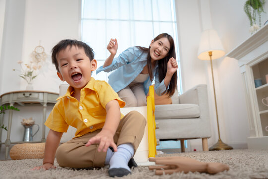 oyful little boy sliding down indoor playground with supportive mother
