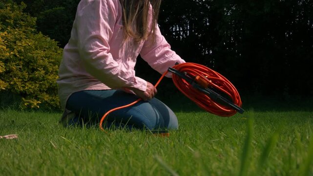 Woman rolling long electric cable in garden grass