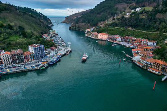 Pasai Donibane, Spain - 10 March 2026: Aerial view of the Harbour mouth of Pasaia with a boat navigating the waterway between colorful houses and lush green hills.