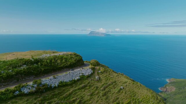 Cinematic Aerial Drone Video of a Dark Car Driving Along a Winding Coastal Highway with Corvo Island on the Horizon, Azores