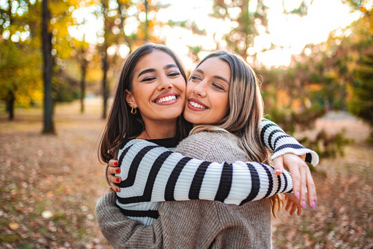 Two girls share a joyful hug in an autumn park filled with colorful leaves