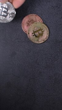 Vertical video of a hand taking a silver bitcoin cryptocurrency coin from stacked gold and copper coins on a dark granite surface, illustrating blockchain technology, digital finance, crypto investmen