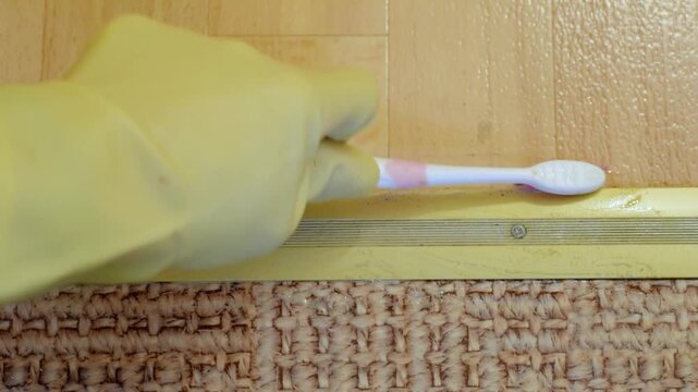 Cleaning metal threshold. Closeup of floor edge cleaning. Hand wearing yellow glove cleans metal threshold edge. Detailed view of glove cleaning residuals from metal threshold edge