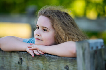 Fototapeta premium Dreamy expression creates soft childhood mood. Green dreamy bokeh surrounds young girl. Dreamy portrait feels warm and peaceful. Dreamy scene supports positive emotion.