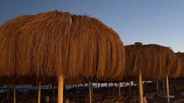 Luxury beach cabanas with straw roofs at expensive resort in Sharm El Sheikh, Egypt. Beautiful Red Sea view in evening twilight. Premium tropical lounge zone. Romantic summer VIP vacation footage.