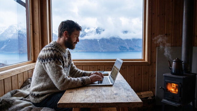 Male Software Developer in Wool Sweater Working on Laptop in Off-Grid Mountain Cabin Overlooking Norwegian Fjord, Remote Work Lifestyle, Cabin Office, Solo Workation