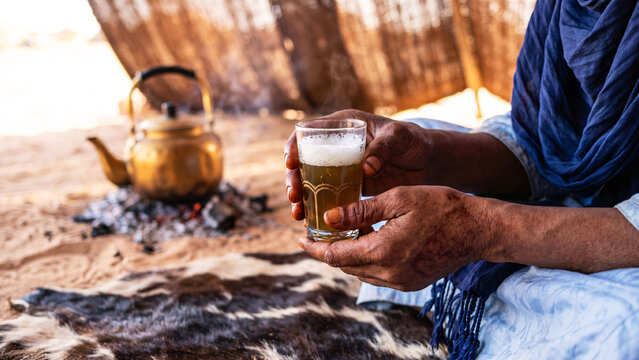 Tuareg Artisan Henna-Darkened Hands Holding Ornate Glass of Saharan Mint Tea on Woven Rug in Desert Tent Near Agadez Niger, North African Culture, Nomadic Tradition