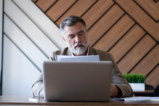 Mature businessman working with document in modern office, reading contract, analyzes graph