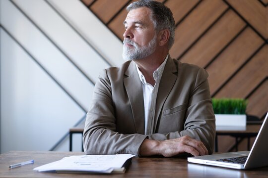 Smiling mature business man executive wearing shirt sitting at desk using laptop. Happy busy professional middle aged manager investor working on computer looking away in office