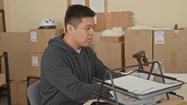 Man with hands clasped on chest at desk among parcel boxes in building packing area; small business pride.