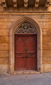 Pietraperzia, Italy. The yellow-ochre colored facade of an old city building. A massive door with ornate decorative elements inside the stone portal.