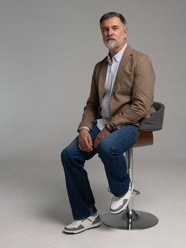 full body picture of happy elegant mature man sitting, laughing in front of white