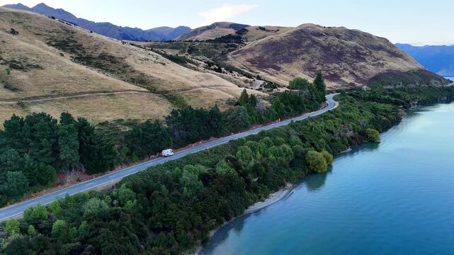 Aerial drone view of Lake Tekapo at sunset, with dramatic alpine scenery in New Zealand. Panoramic landscape of the South Island. A car drives along a scenic road near the Lake Tekapo region. 