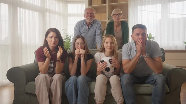 Multigenerational family sitting on couch watching live soccer match, celebrating goal together. Happy grandparents, parents and children supporting favorite team.