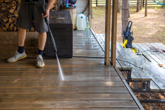 Man pressure washing wooden backyard terrace outdoors, home cleaning detail. Concept: country house maintenance