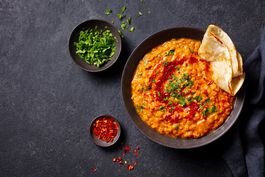 Red lentil dal tadka with flatbread and fresh cilantro on dark grey stone background with copy space. Close up. Top view.