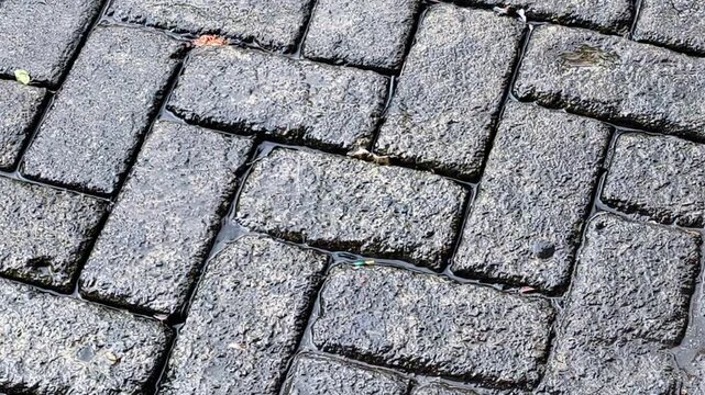 Raindrops on wet herringbone paving. A calming close-up of gentle raindrops splashing on a wet herringbone-patterned stone path. Perfect for a calming visual or relaxing natural setting.