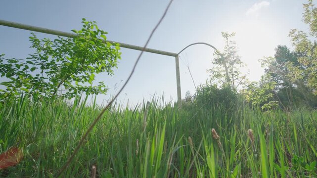 Low-Angle Bottom-Up View: Abandoned Soccer Goal Post Overgrown with Tall Grass | Old Rusty Football Gate Without Net on Neglected Field | Forgotten Sport Infrastructure