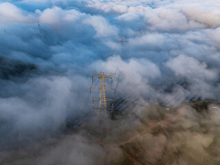 Fototapeta premium High voltage transmission tower standing amidst a sea of clouds in the mountains
