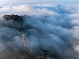 Fototapeta premium High voltage transmission towers standing above the sea of clouds and mountains