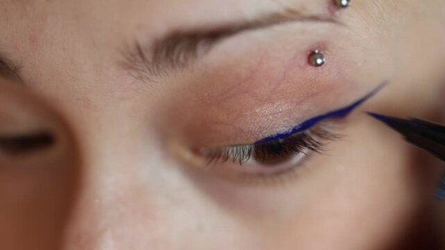 Extreme close up of a woman's eye while applying blue winged eyeliner for a dramatic makeup look