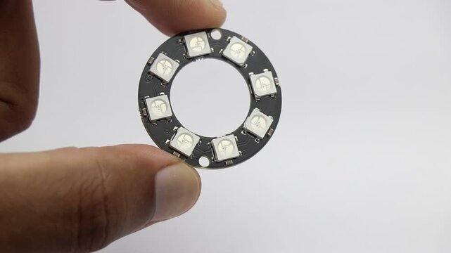 Pixel ring light with 8 RGB Led that is individually addressable using the microcontroller is held in the hand on a white background