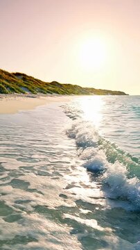 Golden sand beach with lush green dunes dotted with tiny wildflowers and small pebbles. Gentle ocean waves lap the shore under a clear pastel sky as the sun sets, casting a warm glow on the landscape.