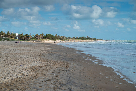 Wide sandy beach with ocean waves and scattered people in the distance in Costa Ballena, Chipiona, C&aacute;diz, Spain.