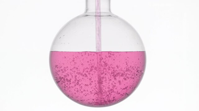 Soft pink transparent liquid injected with long dropper into round-bottom flask, making swirls and bubbles on white backdrop | Roselle tea infusion cosmetic product ingredient concept