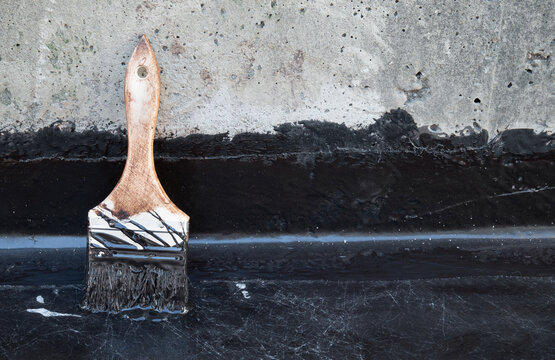 Brush used for liquid membrane application. Close up. Fluid applied liquid coating on concrete floor with vertical upturn detail. Exterior leak repair on balcony, patio or foundation. Selective focus.