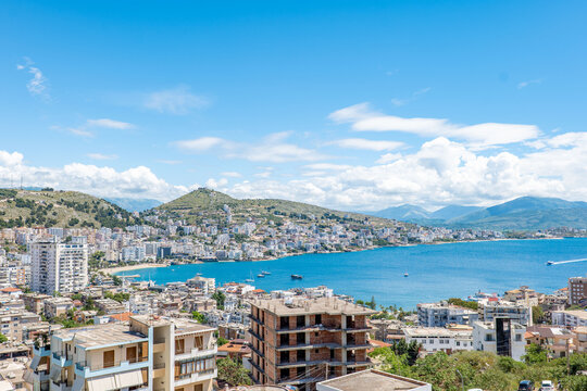 Wide panoramic view of Sarand&euml;, Albania, featuring the Ionian Sea, coastal urban landscape, mountains, blue sky, and summer clouds. Scenic destination on the Albanian Riviera.