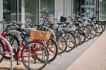 Fototapeta premium Row of bicycles parked outside a modern building, featuring a red bike with a wicker basket and various other styles