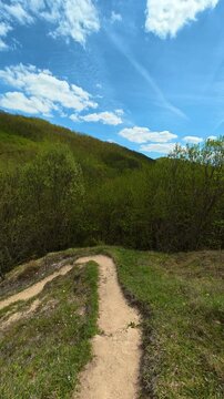 Winding dirt path cuts through grass. Bigar Waterfall, Serbia. Vertical