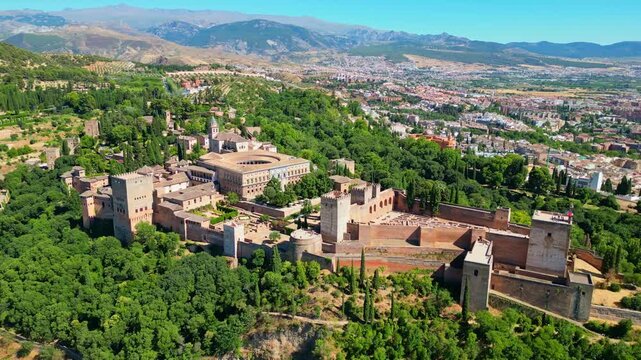 High angle view of the historic Alhambra palace complex and Alcazaba fortress in Granada. Famous UNESCO medieval Moorish architecture surrounded by scenic Andalusian mountains in Spain.