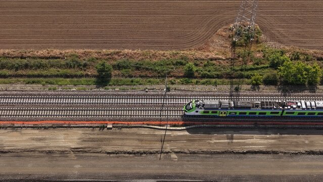 Aerial View of a High-Speed Train on Tracks: An overhead perspective captures a modern, green and silver high-speed train moving along parallel railway tracks, bordered by fields and vegetation.