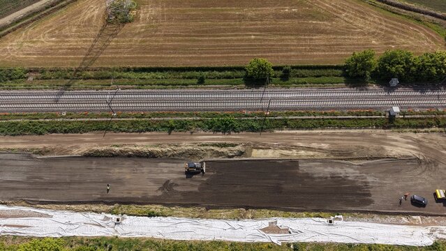 Construction Site Aerial View: An aerial perspective showcases a busy construction site with heavy machinery grading the earth beside a highway, signifying development and progress.