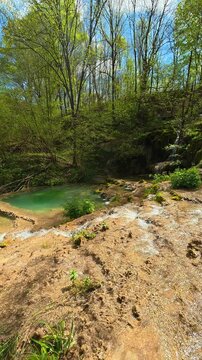 Sunlight filters through green trees above. Bigar Waterfall, Serbia. Vertical
