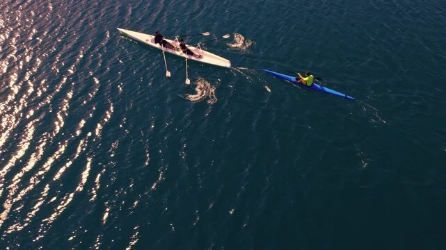 Drone shot of kayakers and rowers moving across sunlit lake water with bright reflections and ripples. Scenic outdoor sport scene showing teamwork, training, freedom and nature.