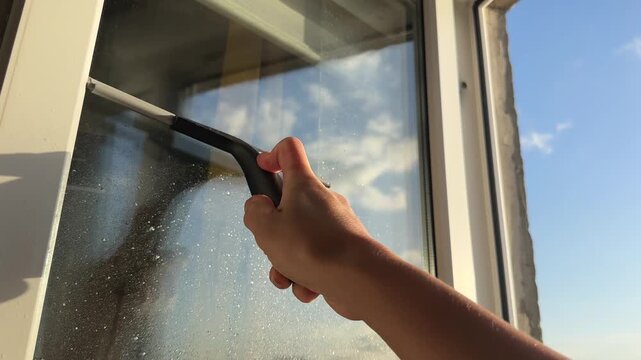 Spring cleaning, female hand using squeegee on sunny window, household chore, home refresh, authentic domestic routine, cleanliness and fresh start concept.