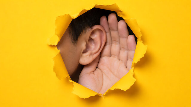 Person's Ear Listening Through a Torn Yellow Paper Hole