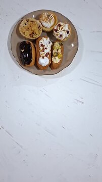 Eclairs Arranged on Plates, Viewed from Above. Vertical Video of Delicious Pastries with Various Toppings and Flavors