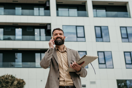 Realtor talking on phone in front of modern apartment building