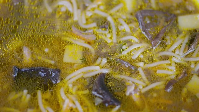 Golden mushroom noodle broth simmering gently rich umami soup with oil droplets, sliced mushroom pieces, thin noodles, potato cubes, warm kitchen glow, closeup simmering shot