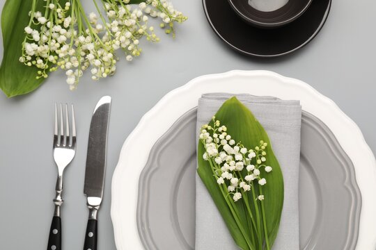 Stylish table setting with plate, cutlery, cup and lily-of-the-valley flowers on light grey background, flat lay