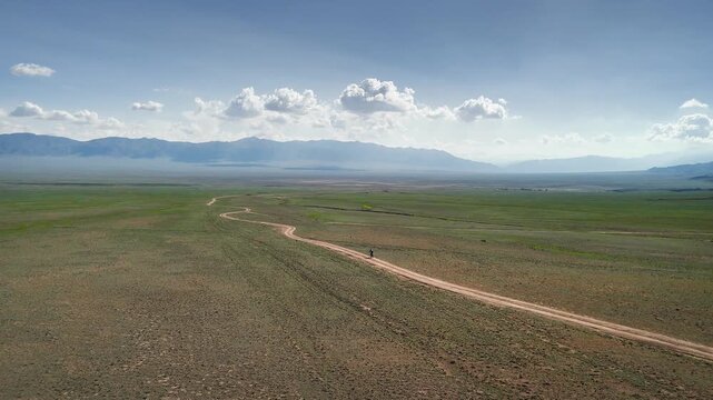 Drone shot of bicycle rider at country road at spring steppe in Kazakhstan