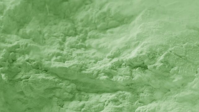 Macro slow-motion capture of fractured pale green powder surface being blown with a strong air stream, breaking its structure and chipping it into small pieces