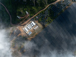 Fototapeta premium Aerial view of mountain solar power station and substation surrounded by clouds and forest