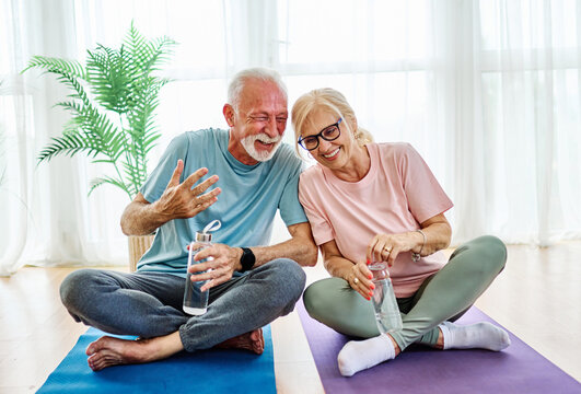 Portrait of a senior couple  holding water bottle and exercise mat smiling and talking at home healthy living