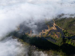 Fototapeta premium Aerial view of solar power station in mountains covered by clouds and fog